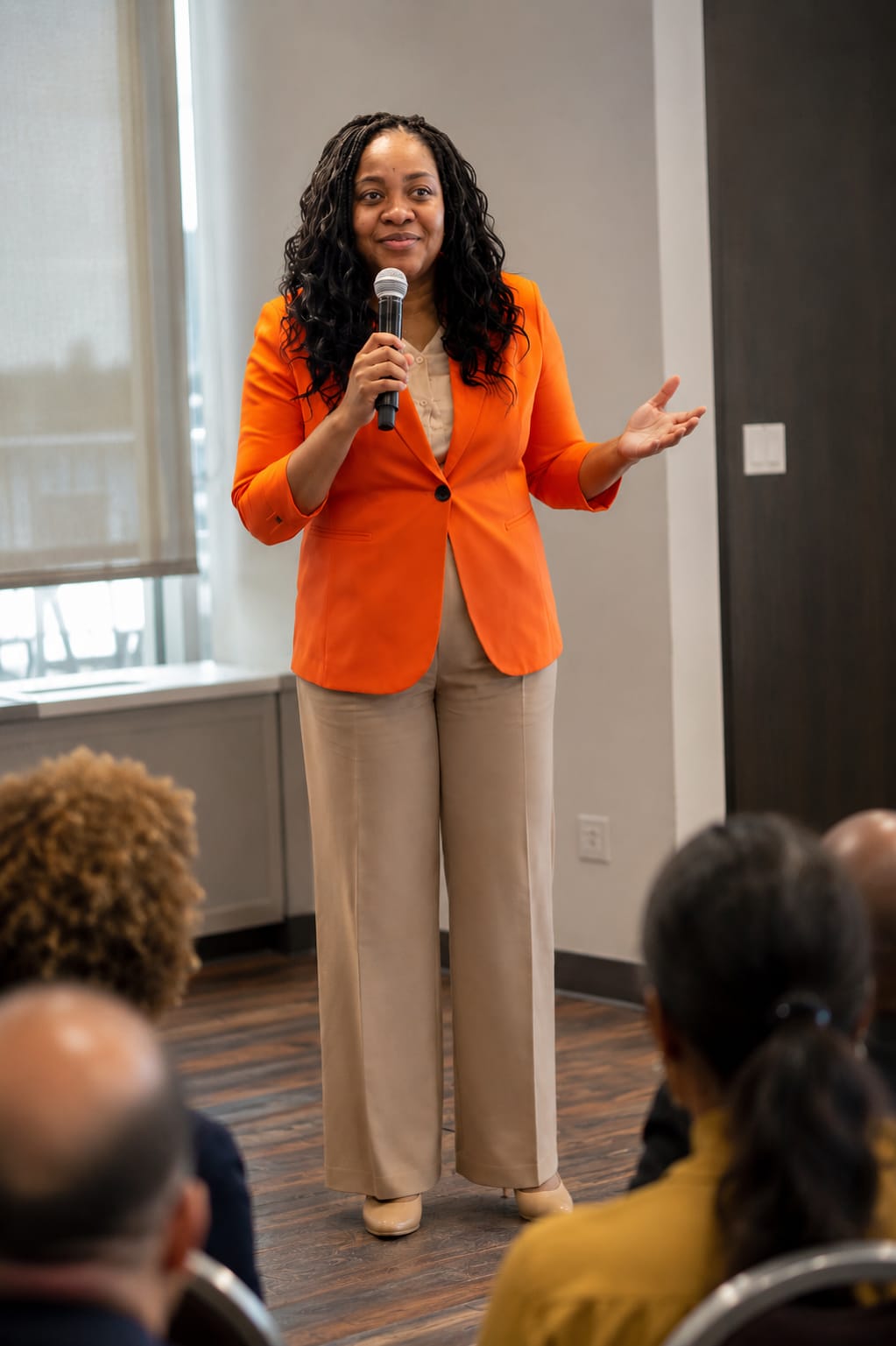 Nadia in an orange blazer holding a microphone and speaking directly to a seated audience