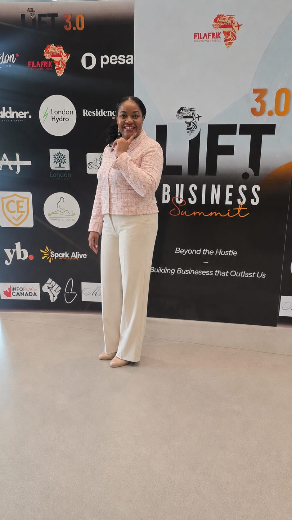 Nadia in a pink jacket standing in front of the LIFT 3.0 Business Summit backdrop